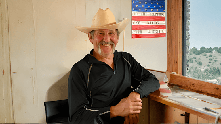 "David Hamel, U.S. Air Force veteran and marathoner, smiling in a cowboy hat, with an American flag in the background."