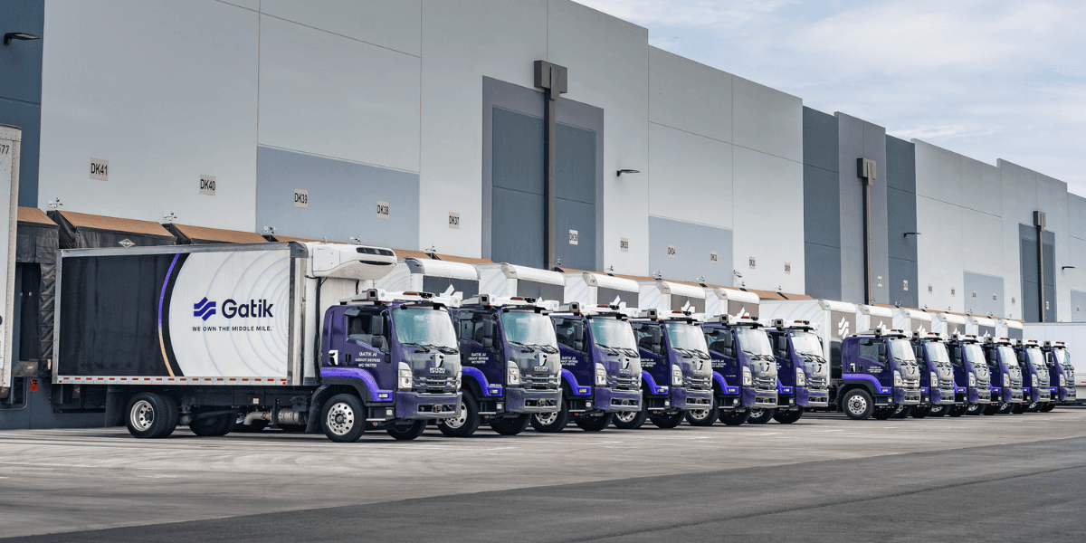 A fleet of autonomous delivery trucks lined up alongside a warehouse loading dock