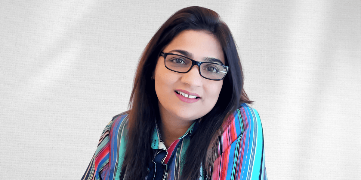 A woman with glasses and colorful striped shirt smiling against a light background