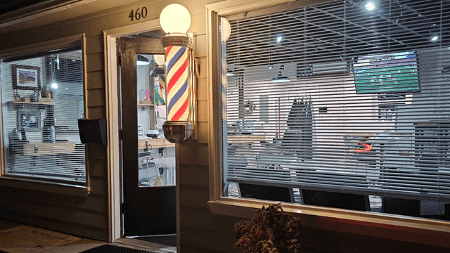 Exterior of Quincy Barbers with illuminated barber pole and storefront entrance at night.