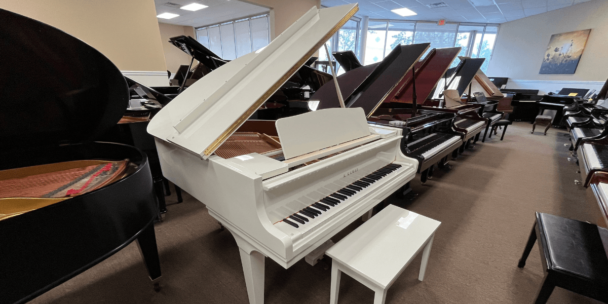 White Kawai grand piano on display in showroom surrounded by other grand pianos for sale.