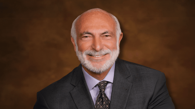 Smiling portrait of author and pediatric cardiologist Michael J. Cooper in a suit against a brown backdrop.