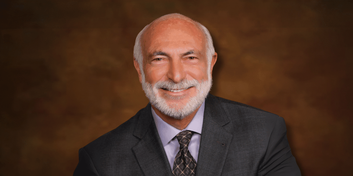 Smiling portrait of author and pediatric cardiologist Michael J. Cooper in a suit against a brown backdrop.