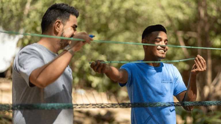 Two volunteers smiling while setting up netting outdoors at The Monkey Farm community project in Costa Rica.