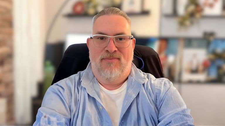 Micheal Franklin, a bespectacled man with a beard, sits in front of a computer, symbolizing his commitment to mental health counseling.
