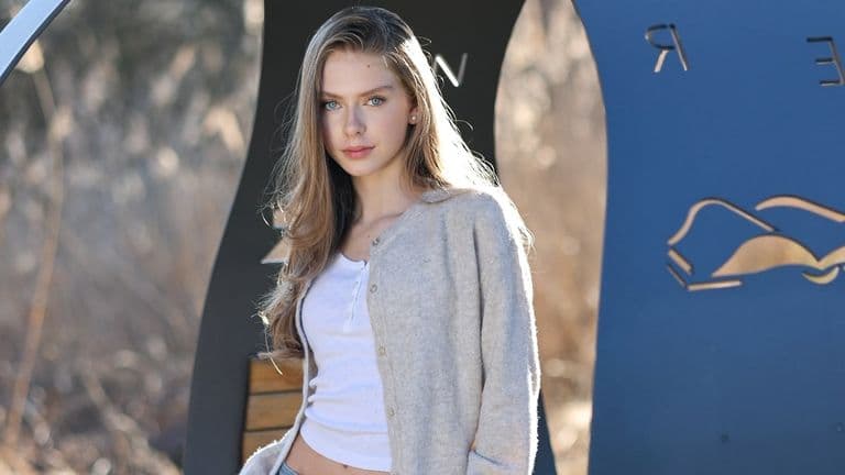 A young woman with long hair in a cardigan poses against a backdrop of modern geometric shapes, exuding a polished aesthetic.