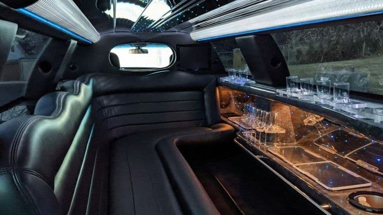 Interior of a luxury limousine featuring sleek leather seating, ambient lighting, and glassware along the bar area.