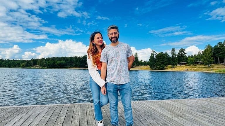 Payal Sood and companion standing on a lakeside dock under a blue sky in Sweden.