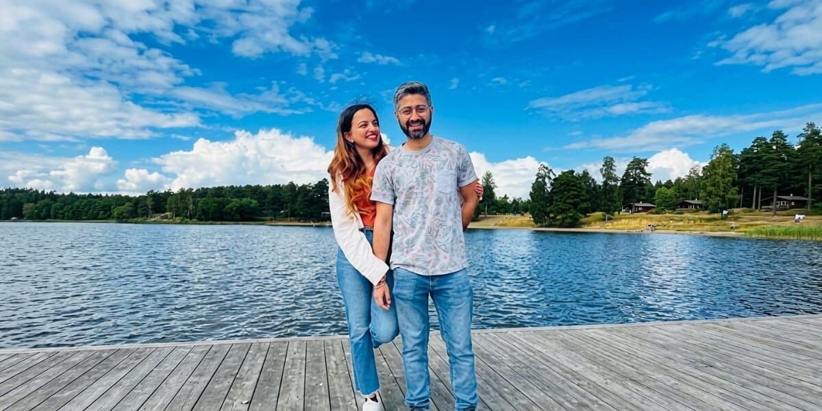 Payal Sood and companion standing on a lakeside dock under a blue sky in Sweden.