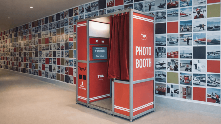 TWA photo booth surrounded by vibrant retro-themed wall of photos, offering a nostalgic interactive experience.