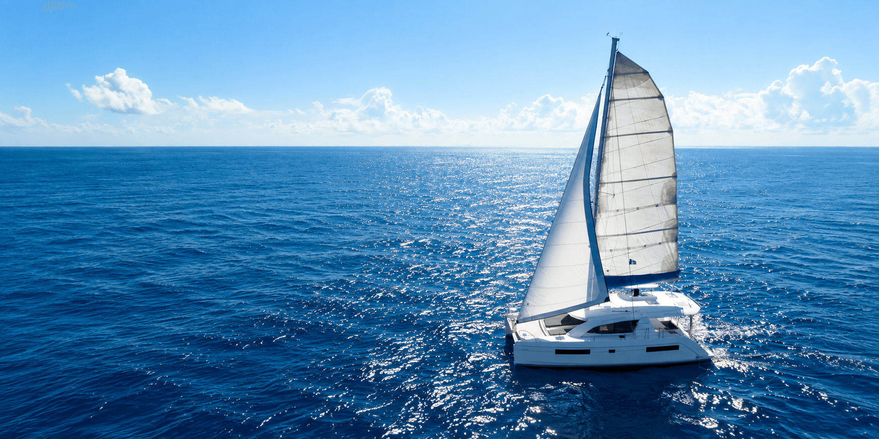 A sailboat with white sails navigating a serene blue ocean under a clear sky