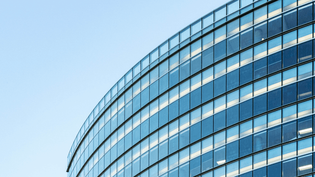 Curved glass facade of a modern building reflecting the blue sky