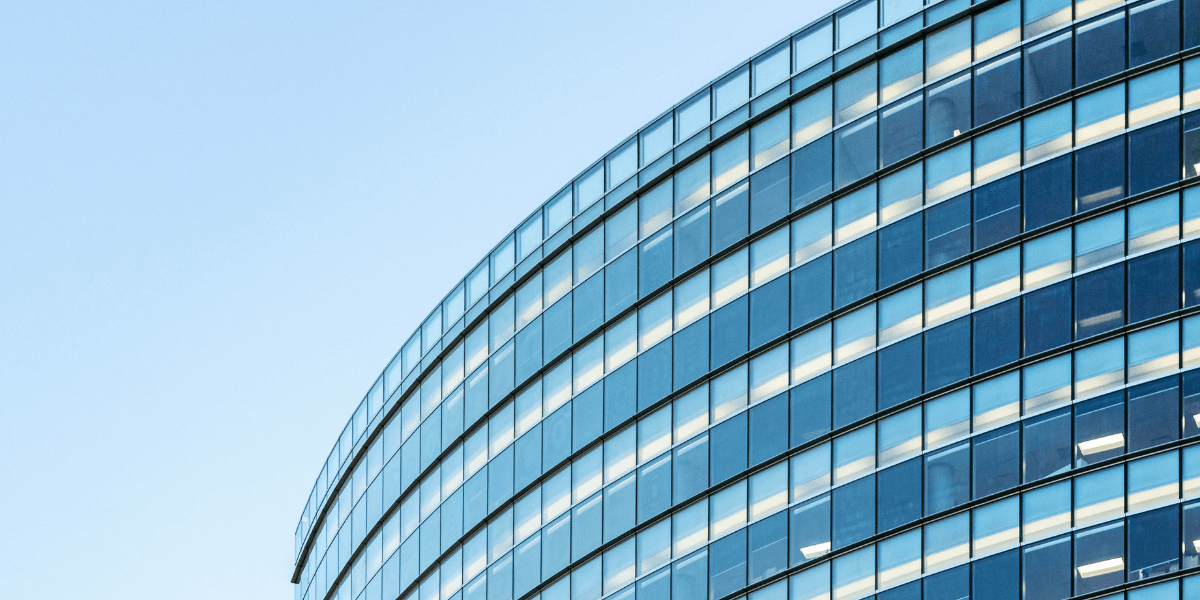 Curved glass facade of a modern building reflecting the blue sky