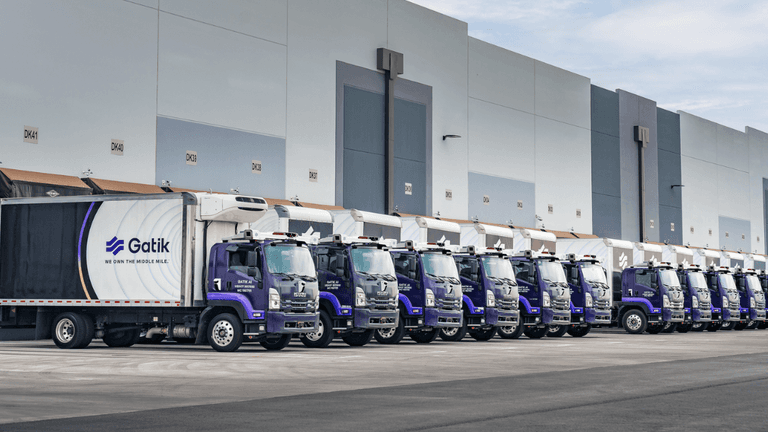 A fleet of autonomous delivery trucks lined up alongside a warehouse loading dock