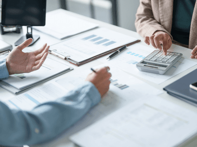 Two people discussing finances with a calculator and paperwork on a table