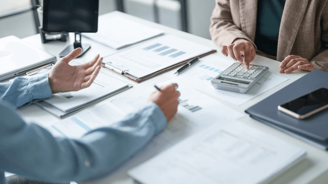 Two people discussing finances with a calculator and paperwork on a table