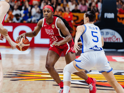 Basketball game with a player in red dribbling while two defenders approach.