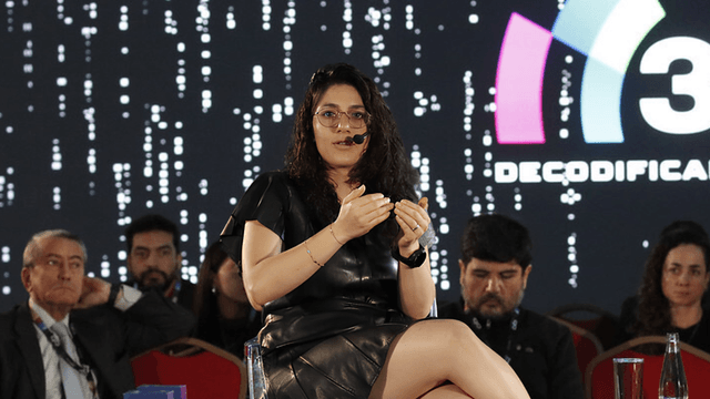 A speaker presents on stage at a conference with an audience in the background