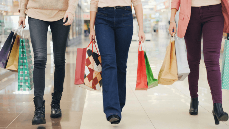Three people walking in a mall, carrying colorful shopping bags.