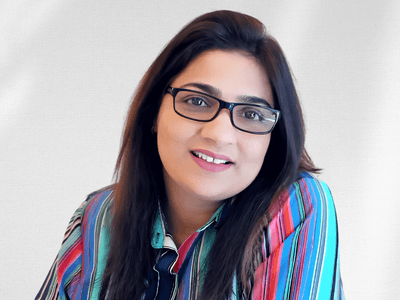 A woman with glasses and colorful striped shirt smiling against a light background