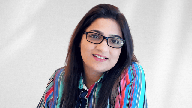 A woman with glasses and colorful striped shirt smiling against a light background