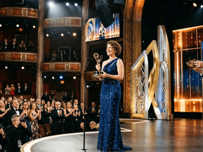 An award recipient in a blue gown stands on stage, holding a trophy amidst applause.