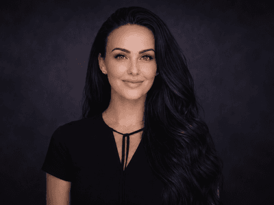A woman with long dark hair and blue eyes smiles against a dark background