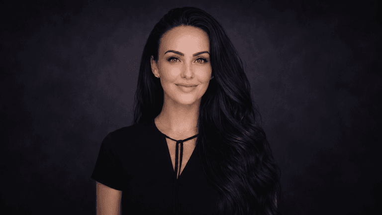 A woman with long dark hair and blue eyes smiles against a dark background