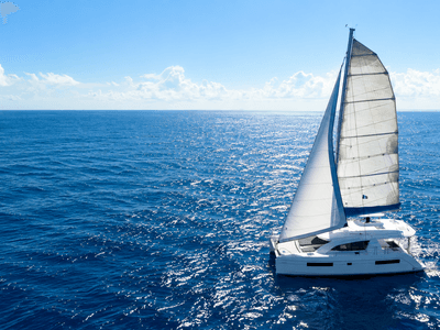 A sailboat with white sails navigating a serene blue ocean under a clear sky