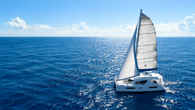 A sailboat with white sails navigating a serene blue ocean under a clear sky