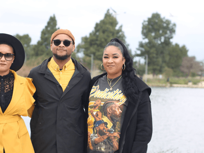 Three individuals posing by a lake, dressed stylishly in colorful outfits.