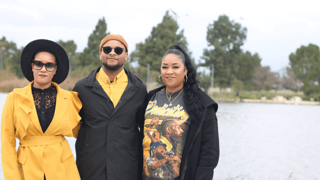 Three individuals posing by a lake, dressed stylishly in colorful outfits.