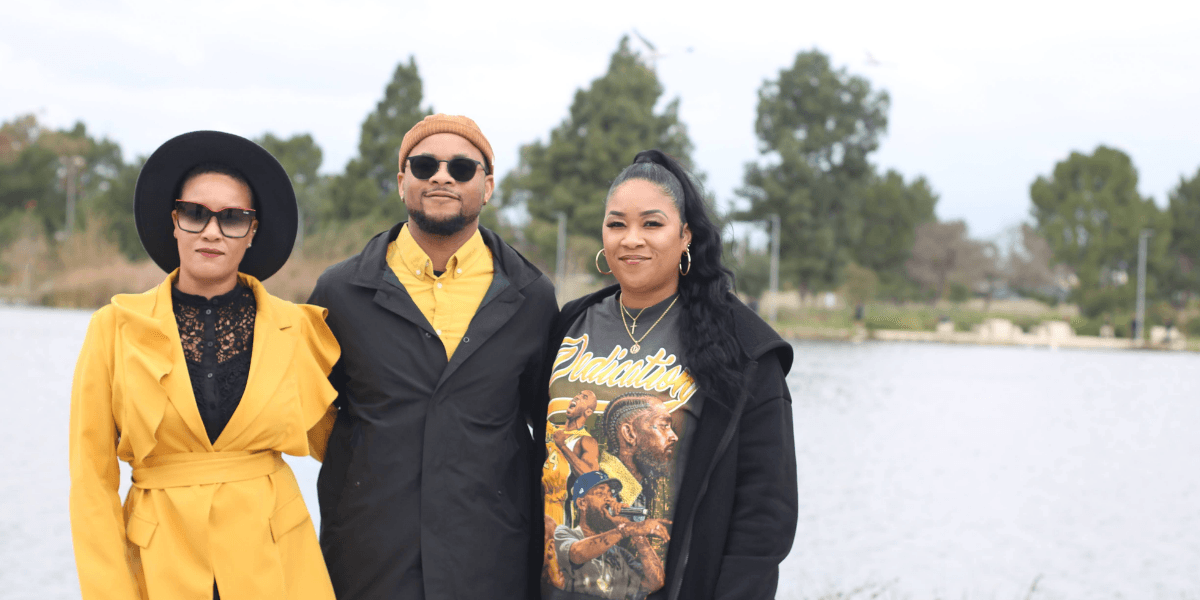 Three individuals posing by a lake, dressed stylishly in colorful outfits.