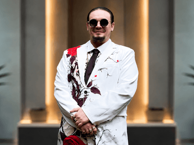 Man in a white suit with red floral patterns and sunglasses, standing confidently indoors