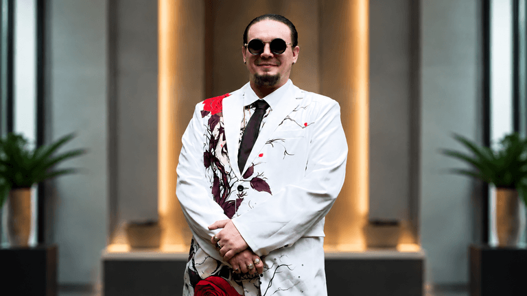 Man in a white suit with red floral patterns and sunglasses, standing confidently indoors
