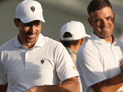 Two smiling men in white polo shirts at a golf event, engaged in conversation