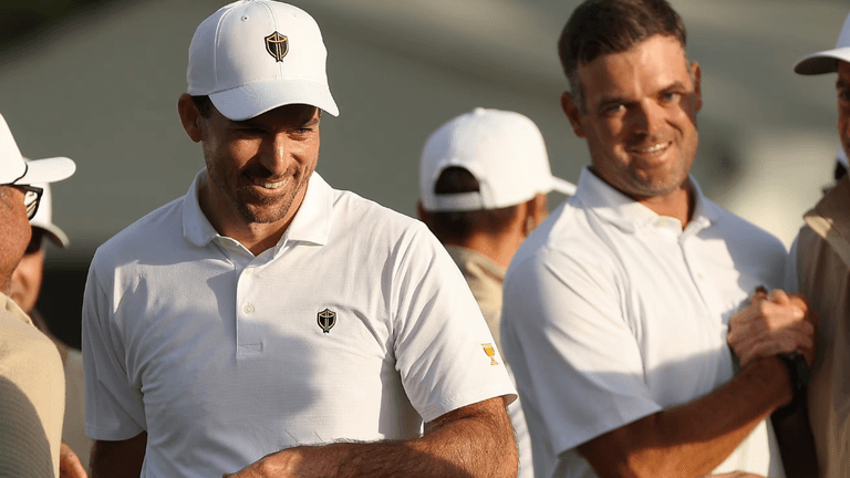 Two smiling men in white polo shirts at a golf event, engaged in conversation