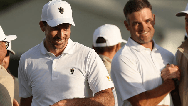 Two smiling men in white polo shirts at a golf event, engaged in conversation