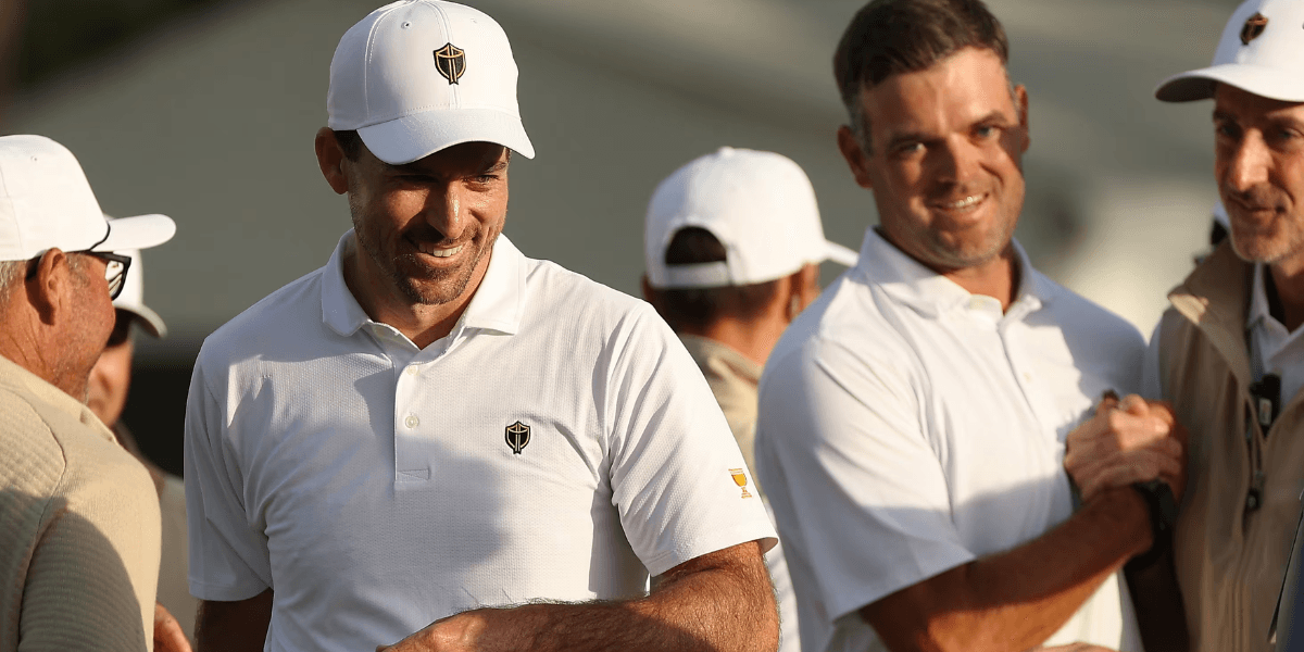 Two smiling men in white polo shirts at a golf event, engaged in conversation