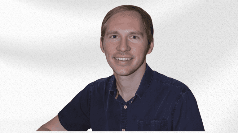 Smiling man with short hair wearing a dark blue shirt against a white background