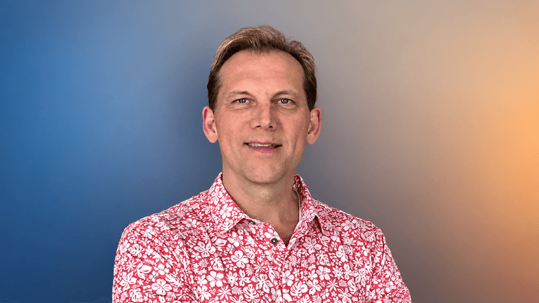 A smiling man in a floral shirt poses against a gradient background