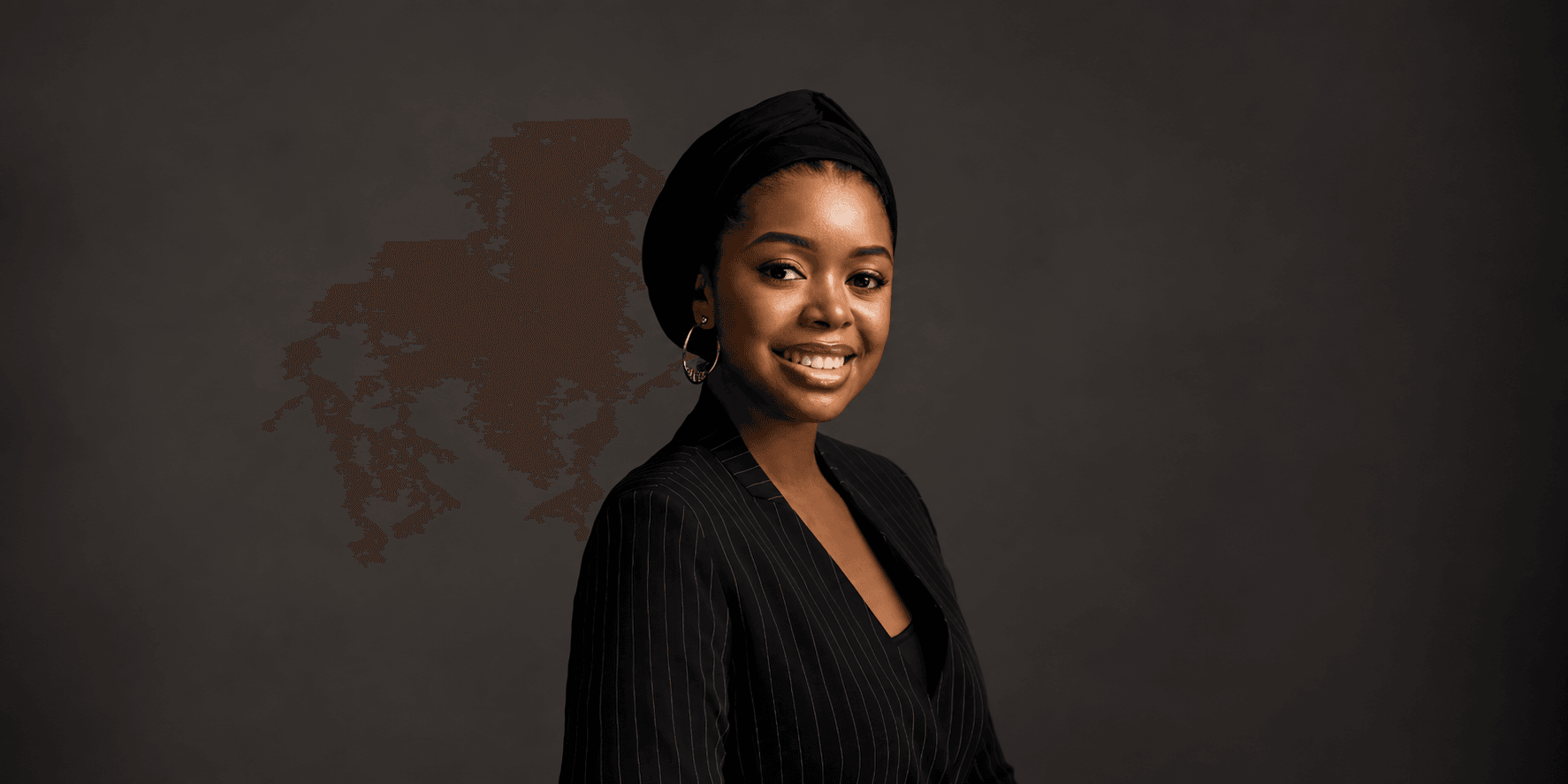 Young woman wearing a black headscarf and pinstripe blazer, smiling against a dark background