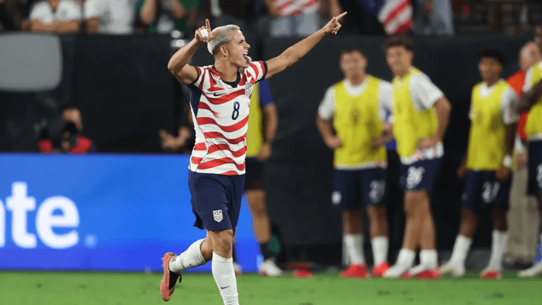 Soccer player celebrating a goal, wearing a striped jersey, with teammates in background