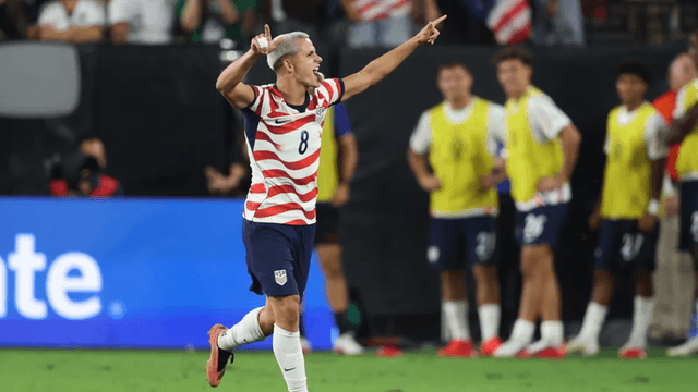 Soccer player celebrating a goal, wearing a striped jersey, with teammates in background
