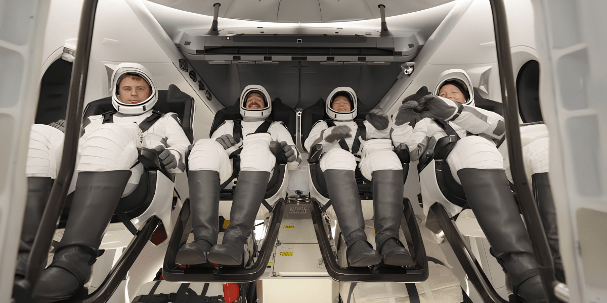 Four astronauts seated inside a spacecraft, wearing space suits and helmets, prepared for launch