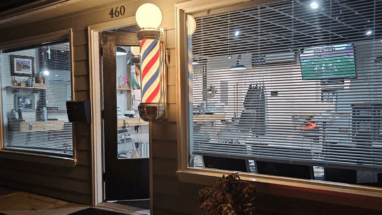 Exterior of Quincy Barbers with illuminated barber pole and storefront entrance at night.