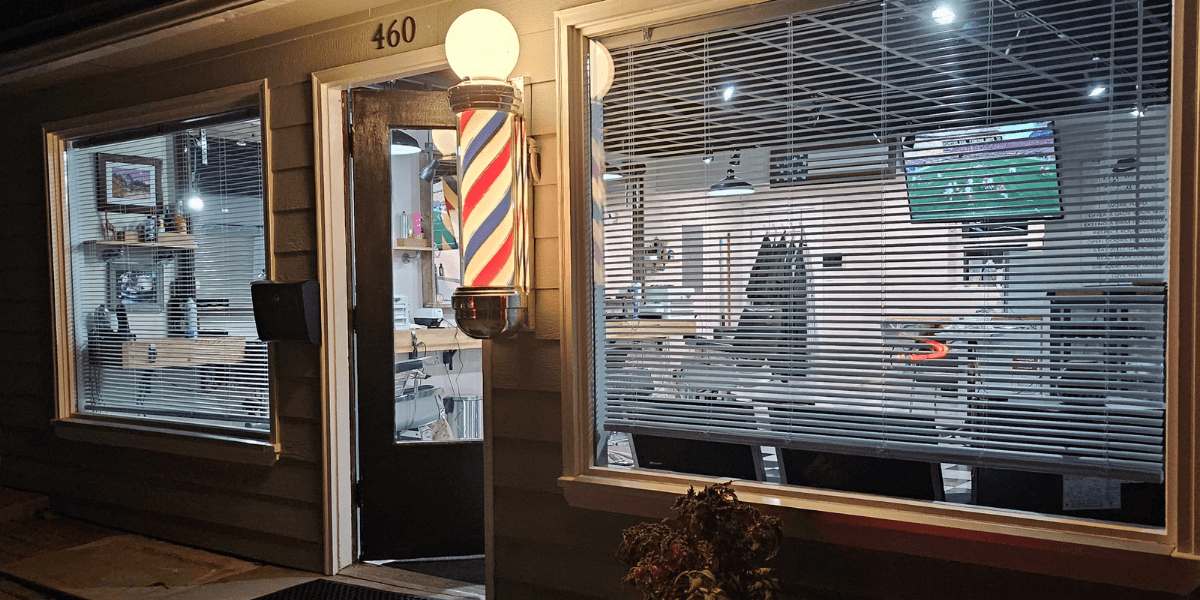Exterior of Quincy Barbers with illuminated barber pole and storefront entrance at night.