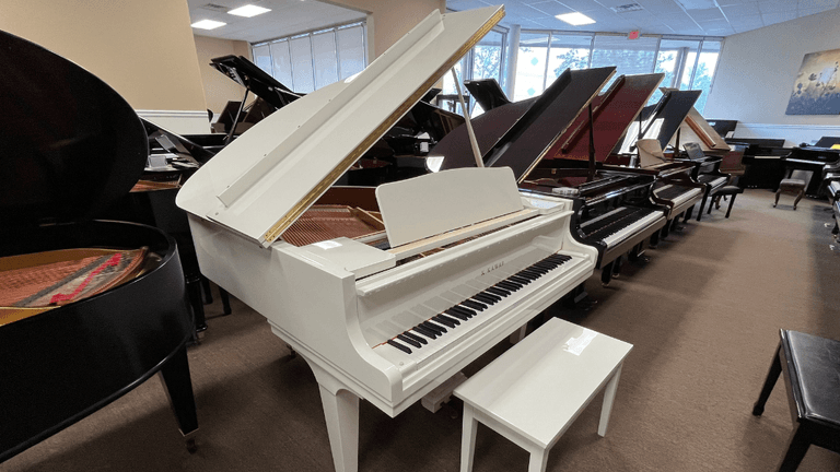 White Kawai grand piano on display in showroom surrounded by other grand pianos for sale.