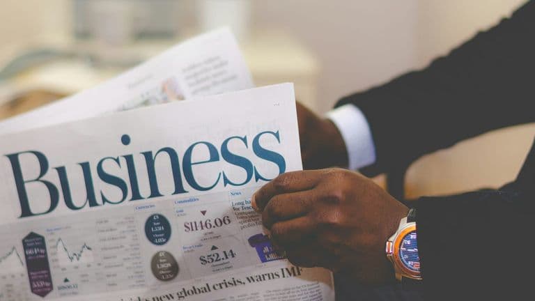 Person in business attire holding a newspaper with financial charts and market information.