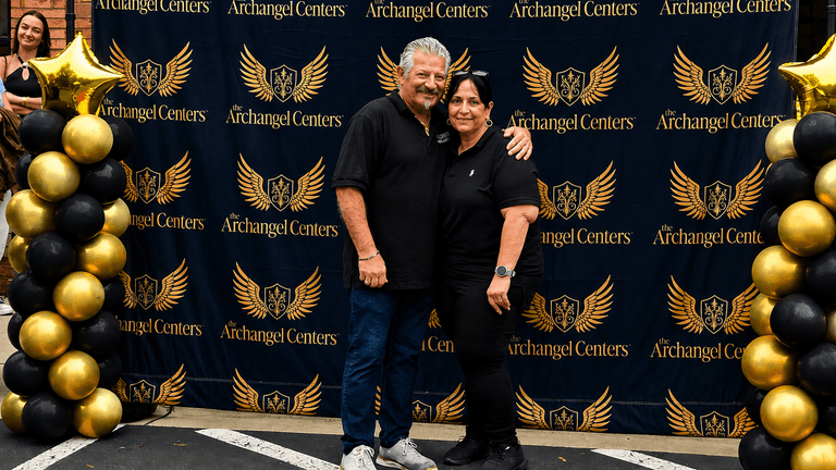 Francesco and Carmela Ventura at an Archangel Centers event with branded backdrop and black-and-gold balloon display.